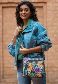 Die mit Blumen bedruckte Umhängetasche zeigt Leoparden, lebendige Blumen und grüne Blätter auf einem schwarzen Hintergrund und hat ein elegantes Design sowie einen verstellbaren Tragegurt.