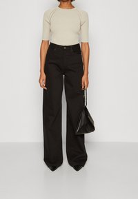 Beige ribbed short-sleeve top paired with high-waisted black wide-leg trousers, featuring a relaxed fit and a smooth texture. Holding a black handbag.