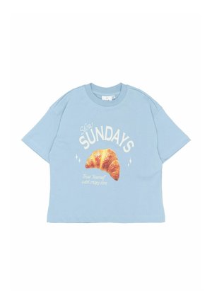 Lyseblå, oversized bomulds t-shirt med korte ærmer. Udstyret med et croissant grafisk design og teksten "Slow SUNDAYS" med yderligere tekst nedenfor.