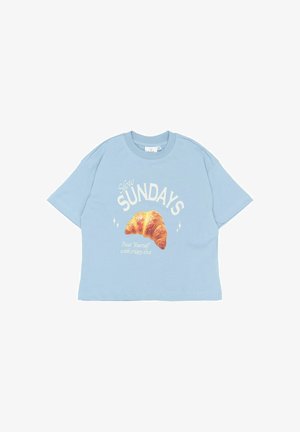 T-shirt en coton oversize bleu clair avec des manches courtes. Présente un graphique de croissant et le texte "Slow SUNDAYS" avec du texte supplémentaire en dessous.