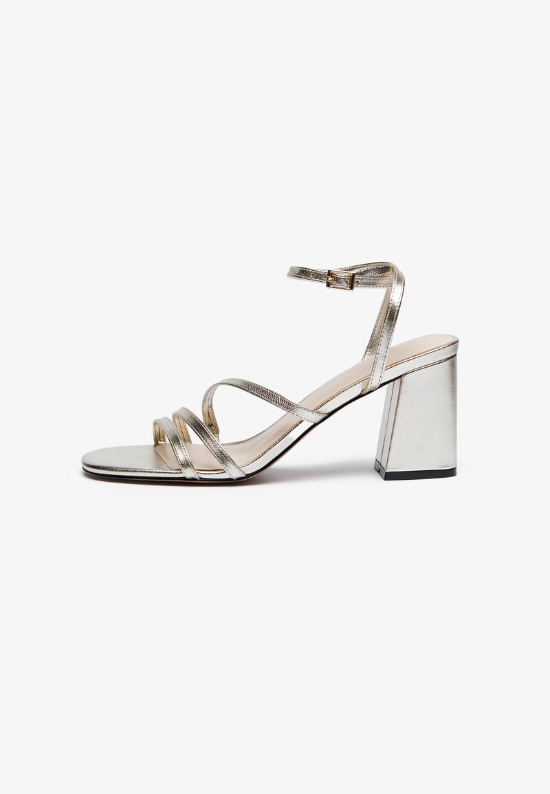 Silver sandaler med band och blockklack. Har metallicmaterial, en ankelrem med spänne och flera tunna remmar över framsidan.