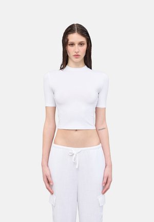 Top blanco recortado con mangas cortas y cuello alto, con una textura suave. Combinado con pantalones blancos holgados de cordón con bolsillos.