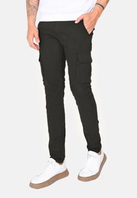 Pantaloni cargo neri a vestibilità slim, dotati di tasche laterali, realizzati in cotone. Indossati con sneakers bianche su uno sfondo neutro.