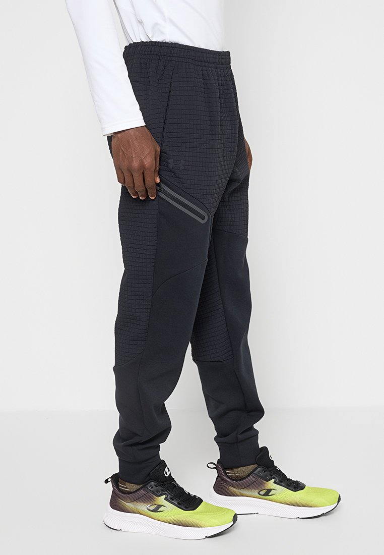 Pantalons de jogging noirs avec un motif texturé, taille élastique, poche latérale zippée et coupe effilée, associés à des chaussures de sport multicolores.