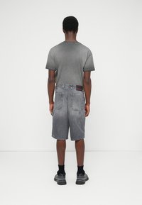 T-shirt grigia a maniche corte abbinata a pantaloncini in denim grigi con finitura sbiadita, molteplici tasche e cuciture a contrasto.