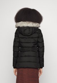 Veste rembourrée noire avec une capuche doublée de fourrure, des poignets élastiqués et une taille cintrée. Présente des panneaux cousus pour la texture et l'isolation.