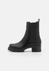 Botín Chelsea negro de cuero con paneles laterales elásticos y suela texturizada. Presenta un tacón bajo y una lengüeta para facilitar su colocación.