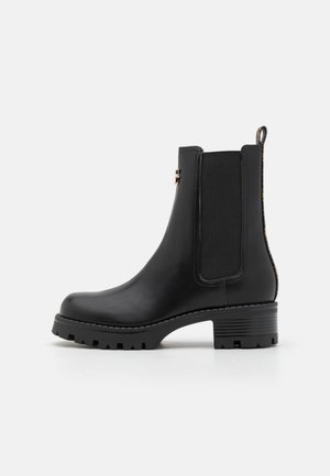 Botín Chelsea negro de cuero con paneles laterales elásticos y suela texturizada. Presenta un tacón bajo y una lengüeta para facilitar su colocación.