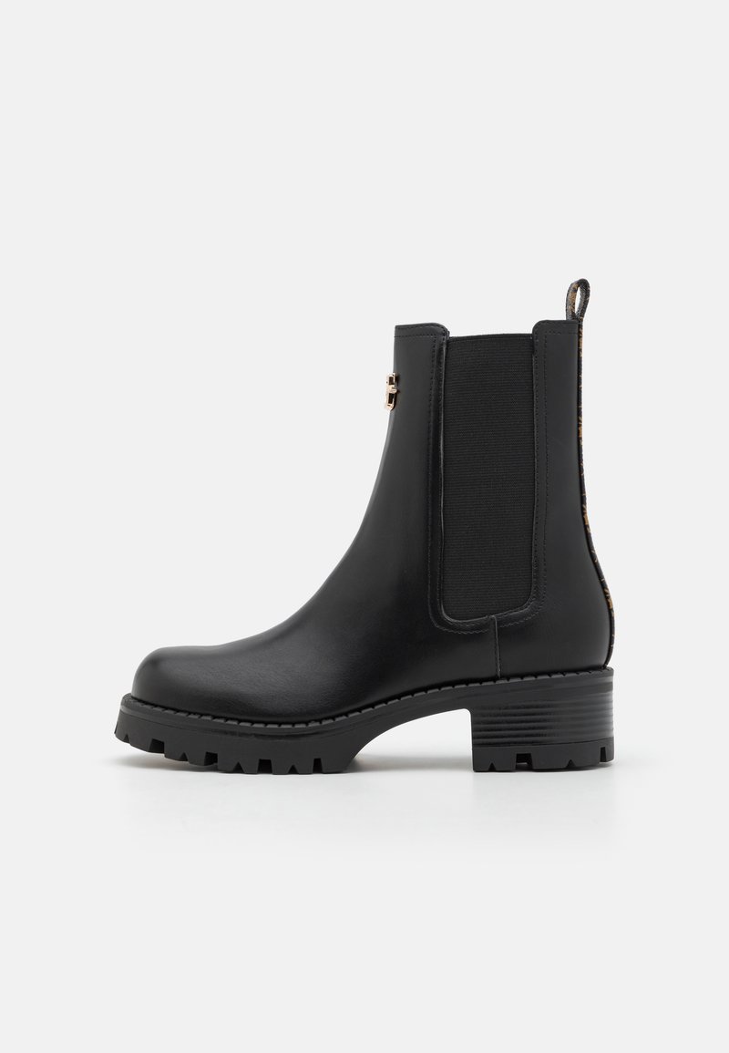 Botín Chelsea negro de cuero con paneles laterales elásticos y suela texturizada. Presenta un tacón bajo y una lengüeta para facilitar su colocación.