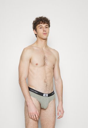 Graue Baumwollunterhose mit schwarzem Bund, der das Logo "Calvin Klein" zeigt. Glatte Textur, taillierte Passform und minimalistischer Stil.