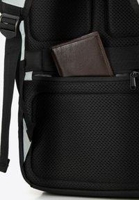 Sac à dos en mesh noir avec un porte-monnaie brun foncé lisse partiellement visible dans une poche extérieure. Couture renforcée et bretelles ajustables.