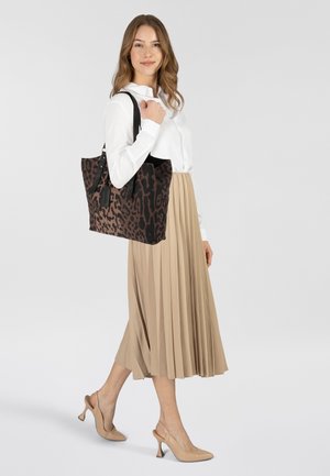 Borsa a tracolla con stampa leopardata realizzata in tessuto, con manici neri. Il modello indossa una camicia bianca e una gonna plissettata beige, abbinata a tacchi beige.