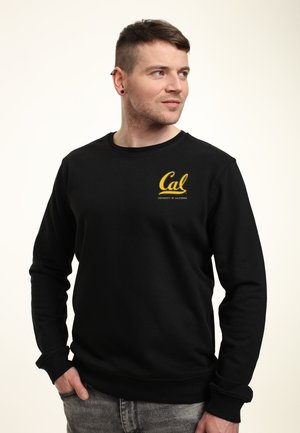 Felpa nera con maniche lunghe, colletto a girocollo e un logo giallo che recita "Cal UNIVERSITÀ DELLA CALIFORNIA" sul lato sinistro del petto.