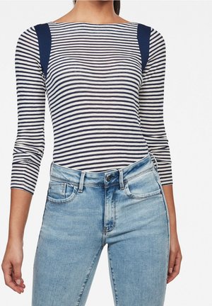 Femme portant un haut à manches longues à rayures horizontales bleu marine et blanc, associé à un jean taille haute bleu clair.