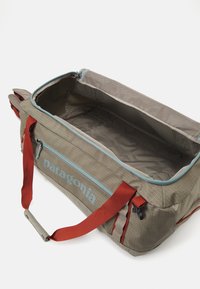 Gray fabric duffel bag with red straps, blue zipper, and woven texture. Interior is spacious and lined, featuring mesh pocket organizer.