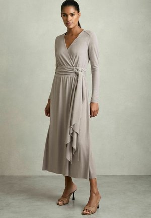 Abito a portafoglio in morbido tessuto beige, con maniche lunghe, scollatura a V profonda e orlo arricciato con dettaglio cintura annodata. Sandali con tacco.