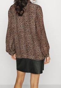Blusa con stampa leopardata e maniche ampie, realizzata in tessuto leggero, caratterizzata da una vestibilità ampia. Abbinata a una gonna in pelle nera.