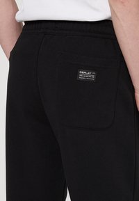 Zwarte sweatpants van een katoenmix, met een achterzak voorzien van een "REPLAY" label. De elastische tailleband zorgt voor een comfortabele pasvorm.