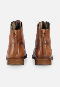 Botas de tobillo de cuero marrón con un acabado liso, cierre de cremallera en la parte posterior y forro textil a rayas en el interior. Suela marrón robusta.