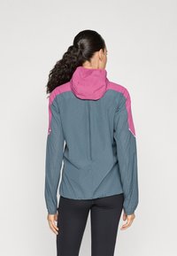 Veste imperméable grise avec des accents roses, dotée d'une capuche, de manches longues et de poignets élastiques. Texture lisse, design léger.