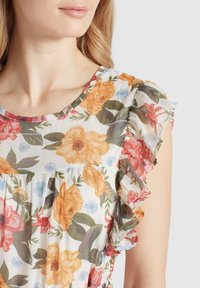 Blommig blus med korta, vågiga ärmar. Vit bakgrund med orange, rosa och blå blommor. Lätt, strukturerad tyg.