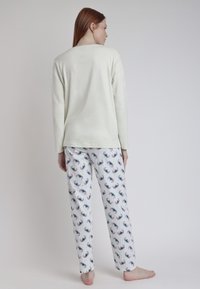 Top de manga larga verde claro combinado con pantalones de pijama blancos a rayas que presentan coloridos patrones de tazas. Tejido suave con un ajuste relajado.