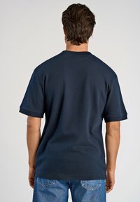 Navy sininen puuvillapaita, jossa on pyöreä kaula-aukko, lyhyet hihat ja rento leikkaus. Silkkinen pinta ja yksinkertainen muotoilu, ilman näkyviä kuvioita.