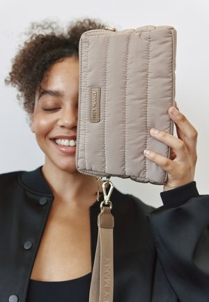 Sac à main beige matelassé avec une texture lisse, quincaillerie dorée et une bandoulière amovible. Présente une étiquette de marque en argent sur le côté.