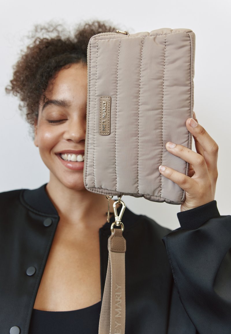 Sac à main beige matelassé avec une texture lisse, quincaillerie dorée et une bandoulière amovible. Présente une étiquette de marque en argent sur le côté.