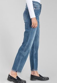 Jean en denim bleu clair avec une coupe droite, texture légèrement délavée, design à cinq poches et ourlet roulé, associé à des mocassins noirs.