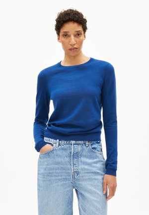 Blauer Pullover mit langen Ärmeln aus weichem Strickmaterial und rundem Ausschnitt, kombiniert mit hellblauen, hochgeschnittenen Jeans.