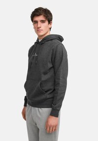 Felpa con cappuccio grigio scuro in materiale felpato, dotata di tasca frontale e cappuccio con cordino, abbinata a pantaloni della tuta grigi chiari.
