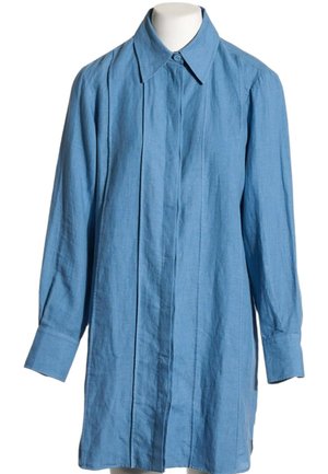 Camisa de lino azul claro de manga larga, con cuello abotonado y tapeta de botones oculta al frente, mostrada en un maniquí.