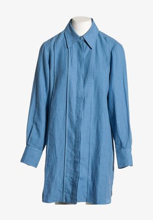 Camisa de lino azul claro de manga larga, con cuello abotonado y tapeta de botones oculta al frente, mostrada en un maniquí.