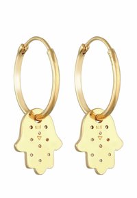 Boucles d'oreilles en or avec un charme hamsa. Le charme présente des découpes et de petites embellissements. Fabriqué en métal, finition polie.