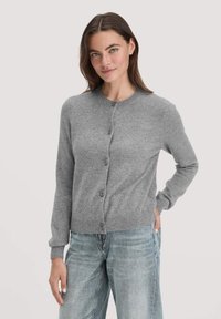 Grau gestrickte Strickjacke mit rundem Halsausschnitt, sieben Knöpfen vorne, gerippten Bündchen und Saum. Kombiniert mit hellblauen Jeans.