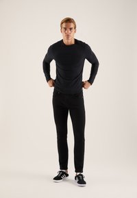 Črna majica z dolgimi rokavi s prileganim krojem, kombinirana s črnimi ozkimi kavbojkami in črnimi supergami z belimi poudarki na podplatu.