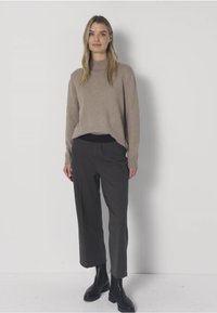 Beige gebreide trui met een hoge hals en geribbelde manchetten, gecombineerd met donkergrijze, wijd uitlopende broek met elastische tailleband en enkellaarsjes.