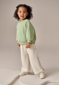 Jasnozielona bluza z bufkami, zestawiona z jasnobeżowymi spodniami wide-leg o splocie z drobnymi wzorami. Całość uzupełniają białe sneakersy.