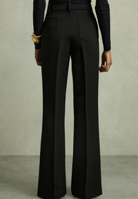 Pantalones de tiro alto negros con un diseño de pierna acampanada, tejido suave y dos bolsillos traseros. Presenta una cinturilla definida y costuras laterales.