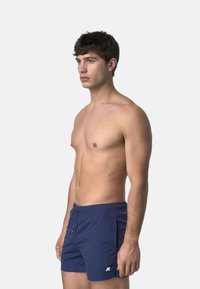 Pantaloni da nuoto blu navy con vita elasticizzata e cordino, realizzati in tessuto leggero; presenta un piccolo logo bianco sul davanti in basso.