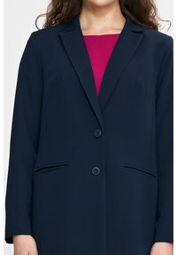 Granatowa marynarka o dopasowanym kroju, z dwoma guzikami, klapkowymi kieszeniami i wyciętymi klapami. Lekka tkanina o gładkiej teksturze.