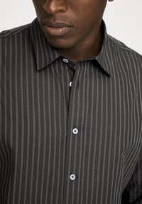 Dunkelgraues Hemd mit Knöpfen und vertikalen weißen Streifen, ausgestattet mit einem klassischen Kragen und weißen Knöpfen, aus einem glatten Stoff.