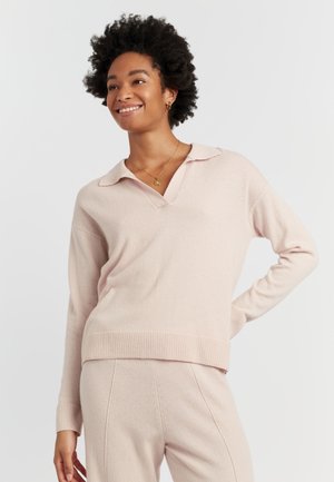 Lichtroze gebreide pullover met een V-hals en kraag, met lange mouwen en geribbelde manchetten, gecombineerd met bijpassende broek. Zachte textuur.