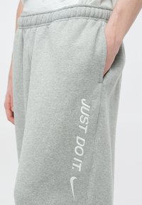 Sive trenirke iz bombažne mešanice, z bočnimi žepi in belim napisom "JUST DO IT." ter majhnim logotipom Nike na levi nogi.