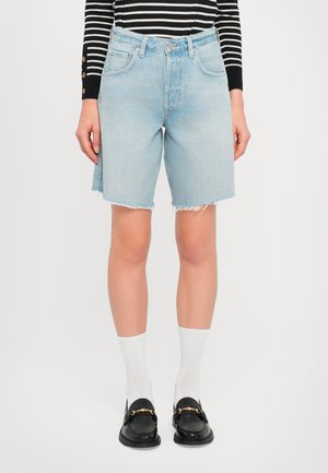 Light blue denim shorts with a high waist, frayed hem, and five-pocket design. Paired with black loafers and white crew socks.