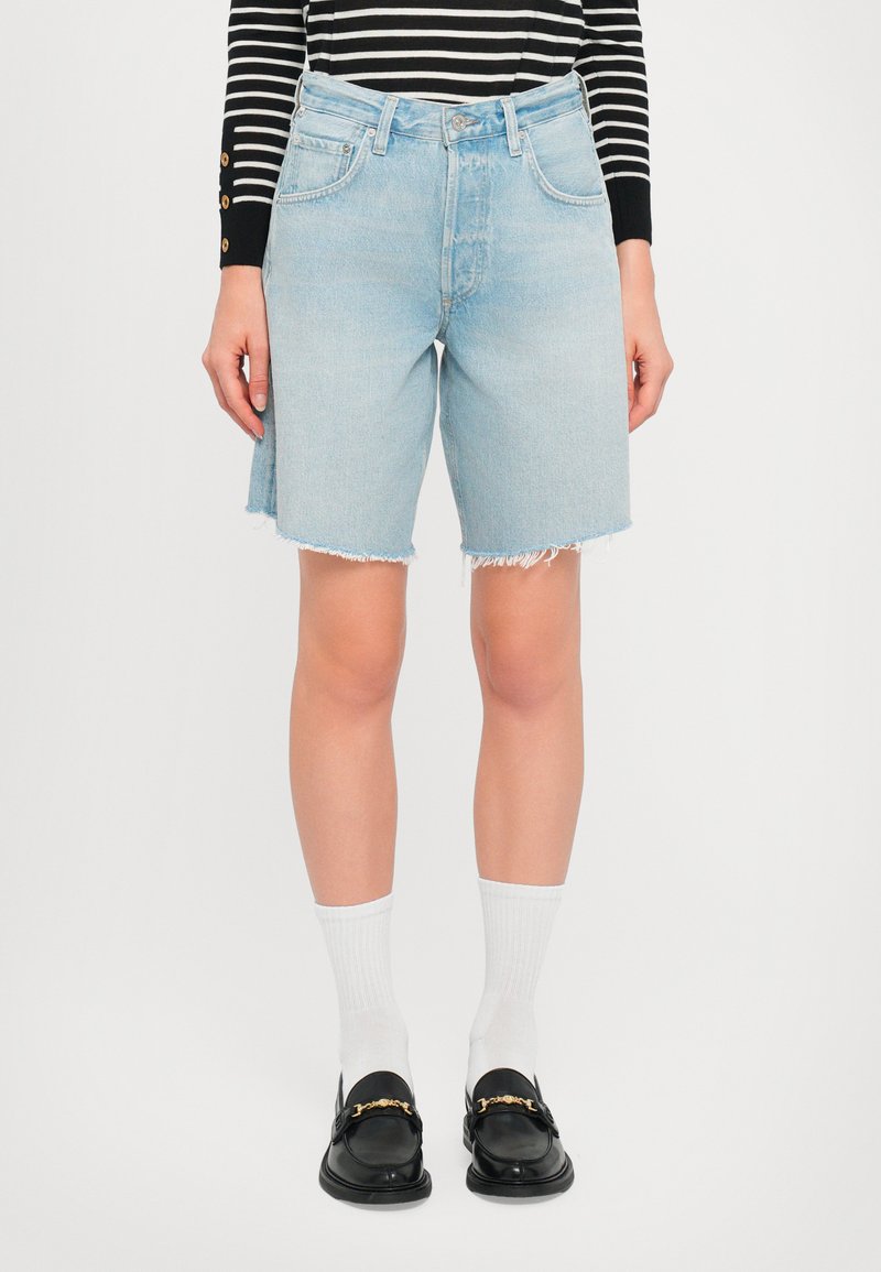 Shorts in denim azzurro chiaro con vita alta, orlo sfrangiato e design a cinque tasche. Abbinati a mocassini neri e calzini bianchi alla caviglia.