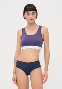 Lila pamut sportmelltartó széles fehér pánttal, melyen a "COPENHAGEN STUDIOS" felirat olvasható, illetve hozzá illő tengerészkék fürdőnadrág, mindkettő sima felülettel.