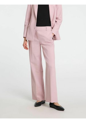 Person iført lyserøde skræddersyede bukser og matchende blazer kombineret med en sort top og sorte flade sko.