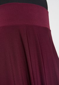 Gonna bordeaux con una cintura larga, pieghe fluide e un tessuto morbido e testurizzato con una lucentezza sottile.